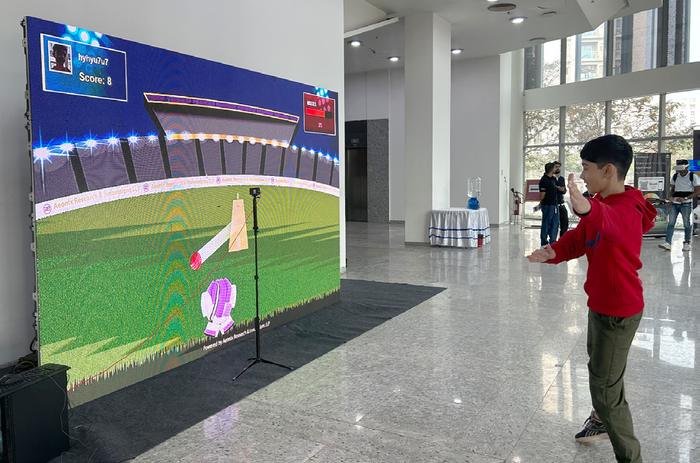 A child playing a gesture-controlled cricket game on a large screen
